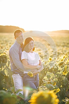 A husband standing near her beatiful wife in the field with lots of sunflowers on a sunny evening