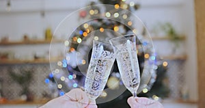 Husband and wife celebrate Christmas by clinking champagne glasses in front of decorated Christmas tree in living room
