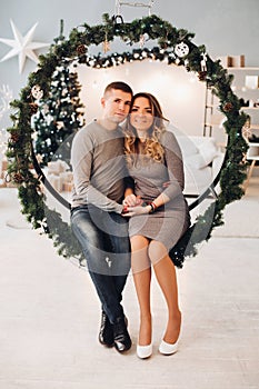 Husband and wife on Christmas swing. Christmas tree.