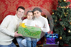 Husband, wife and daugther with gift smile near Christmas tree
