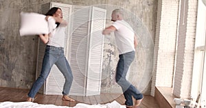 Husband and wife fight pillows and laugh. They are home on self-isolation.