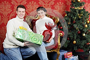 Husband and wife with gifts smile near Christmas tree