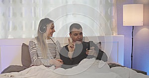 Husband and wife in headphones watching TV in the bedroom.