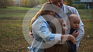 Husband and wife hug their two children in the autumn park. Happy family on a walk. Sunset in the city park