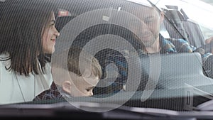 A husband, wife and little son are sitting in a new car. The joy of a new purchase.