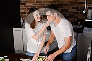 Husband and wife prepare salad together in the kitchen, cut vegetables, woman gives man to try vegetables. Concept of