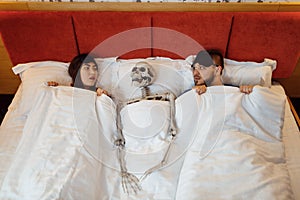 Husband, wife and skeleton lying in the bed