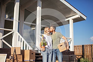 Husband and wife standing in front of new buying home with boxes