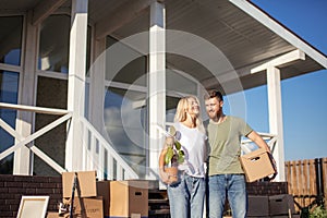 Husband and wife standing in front of new buying home with boxes