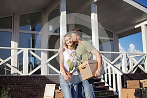 Husband and wife standing in front of new buying home with boxes