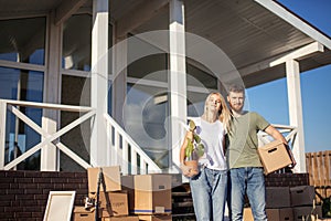 Husband and wife standing in front of new buying home with boxes