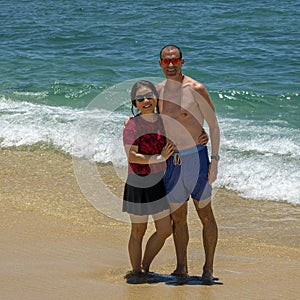 Husband and wife standing in the sand of Medano Beach with the Sea of Cortez in the background in Cabo San Lucas.