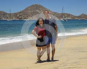 Husband and wife standing in the sand of Medano Beach with the Sea of Cortez and moored boats in the background in Cabo San Lucas.