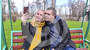 Husband and wife take a selfie while sitting on a swing in the park. Happy couple taking pictures of themselves. The concept of a