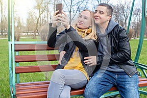 Husband and wife take a selfie while sitting on a swing in the park. Happy couple taking pictures of themselves. The concept of a