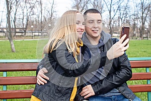 Husband and wife take a selfie while sitting on a swing in the park. Happy couple taking pictures of themselves. The concept of a