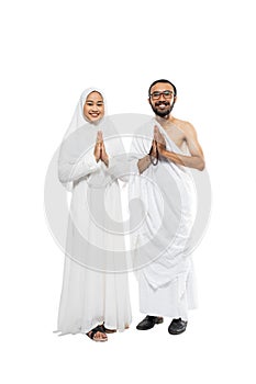 Husband and wife wearing hajj ihram clothes with greeting gesture