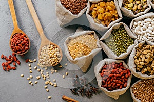 Husbandry and nutrtion concept. Top view of various beans and colorful dried fruit packed in little burlap sacks. Wooden spoon