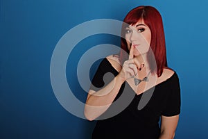 Attractive woman in black dress, red hair making gesture silence