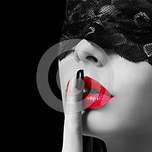 Hush. woman with finger on her red lips showing shush. Erotic girl with lace mask over black background.