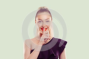 Hush. Woman smiling asking for silence or secrecy with finger on lips shh hand gesture light green background. Pretty girl placing