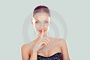 Hush. Woman smiling wide eyed asking for silence or secrecy with finger on lips shh hand gesture light green background. Pretty