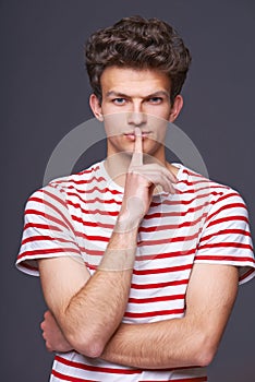 Hush. Young serious sullen man with finger on lips photo