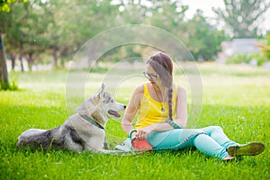 Husky sits with his mistress on a sunny day on the grass