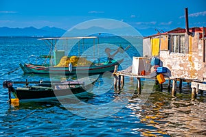 Hut by the seaside. Sunlit small blue, white and yellow Mediterranean fishing boats, with sparkling turquoise sea and pale blue