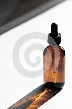 Hyaluronic acid oil mockup with collagen and peptides in brown bottle on white surface with geometric shadows. Skincare photo