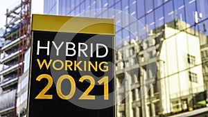 Hybrid Working 2021 on a city-center sign in front of a modern office building