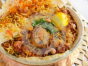 Hyderabadi chicken biryani with tomato, coriander, lemon, cashew nut and bread dum served in copper pot dish isolated on wooden