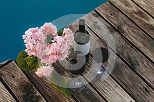 Hydrangea two glasses and a bottle of red wine on the wooden floor near the pool