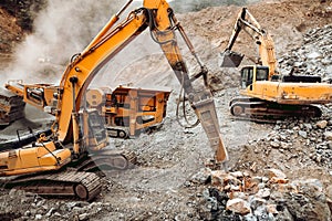 Hydraulic crusher and track type excavator backhoe machinery working. Industrial machineries working on open pit mine, ore quarry