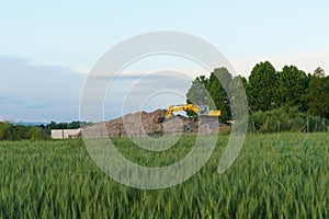 A hydraulic excavator on a pile of crushed construction waste against the backdrop of a green field.