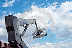 Hydraulic lifting platform with a bucket on a blue  cloudy sky. Building. Industry. Construction machinery