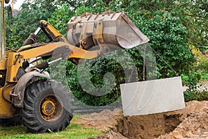 Hydraulic piston system of the excavator with a bucket, lowering into the pit on steel cables concrete sewer ring. Construction or