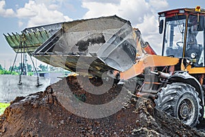 Hydraulic piston system of the excavator with a bucket, lowering into the pit on steel cables concrete sewer ring. Construction or