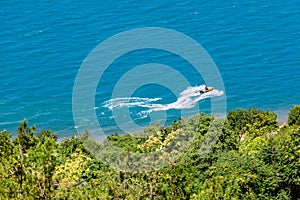 The hydrocycle rides on blue water along the green shore with trees.