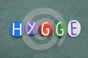Hygge, danish word, fun, composed with multi colored stone letters over green sand
