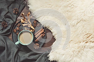 Hygge still life with hot cup of black coffee, anise, warm scarf on furskin and wooden board. Copy space. Top view.