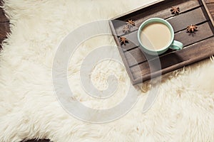 Hygge still life with hot cup of black coffee, warm scarf on furskin and wooden board. View from above