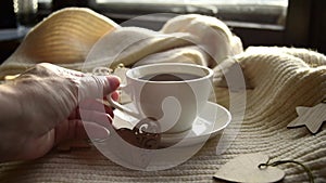 Hygge style. Woman's hand takes a mug of black coffee wrapped in a warm scarf with wooden Christmas decorations