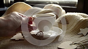 Hygge style. Woman's hand takes a mug of black coffee wrapped in a warm scarf with wooden Christmas decorations