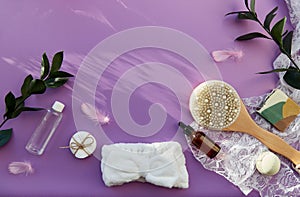 Hygiene accessories, natural soap, essence oil, massage brush, bath bomb, sponges on purple background. SPA beauty
