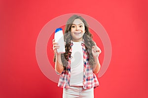 Hygiene habits for kids. Happy little girl holding gel or shampoo bottle for personal hygiene on red background. Small