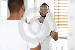 Daily Hygiene. Handsome Black Man Wiping Face With Towel In Bathroom