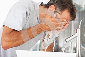 Hygiene, hydration and a man washing his face in the bathroom of his home in the morning to wake up. Fresh, water and