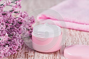 Hygienic cream skincare product  in pink plastic jar with towel on white table