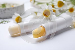 Hygienic lipsticks and chamomile flowers on background, closeup